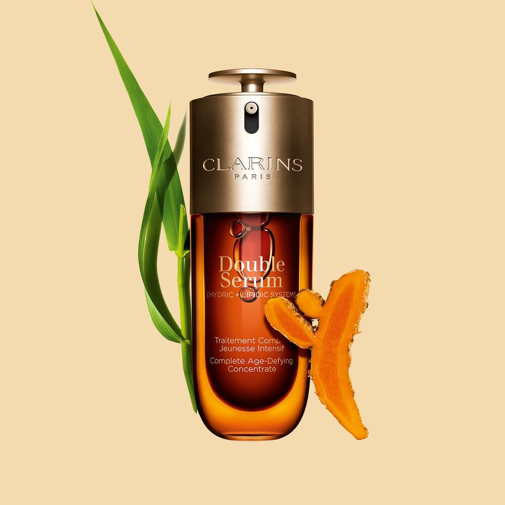 Packshot des Clarins Double Serum vor den Inhaltsstoffen, darunter Kurkuma, vor einem goldenen Hintergrund