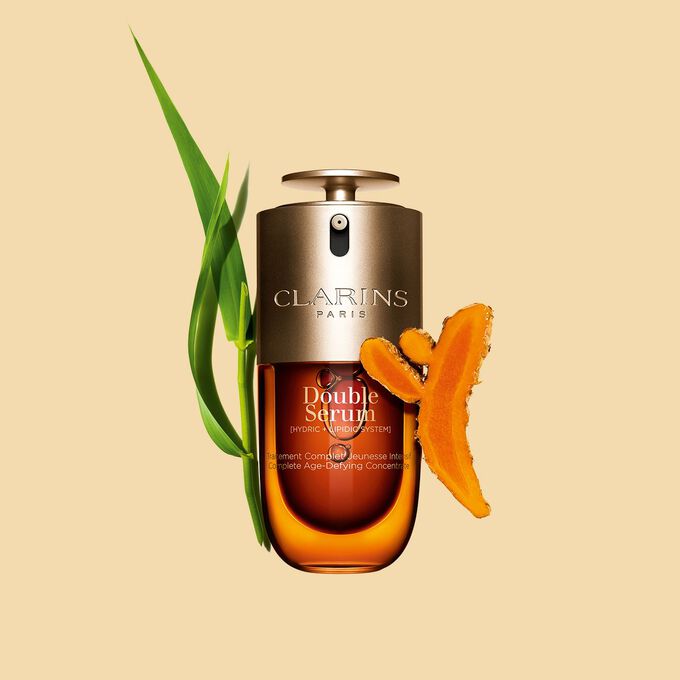 Packshot des Clarins Double Serum vor den Inhaltsstoffen, darunter Kurkuma, vor einem goldenen Hintergrund