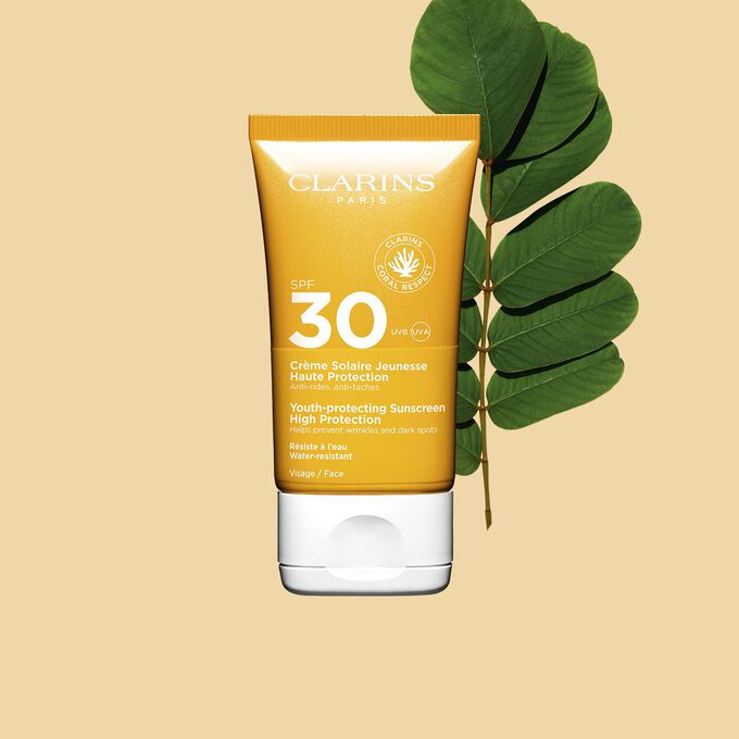 Packshot einer orangefarbenen Tube Sonnencreme SPF 30 neben einem Sennesblatt vor einem hellorangen Hintergrund