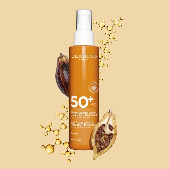 Packshot eines dunkelorangen Sprays Body Lotion mit Sonnenschutz SPF 50 neben Kakaobohnen vor einem hellorangen Hintergrund