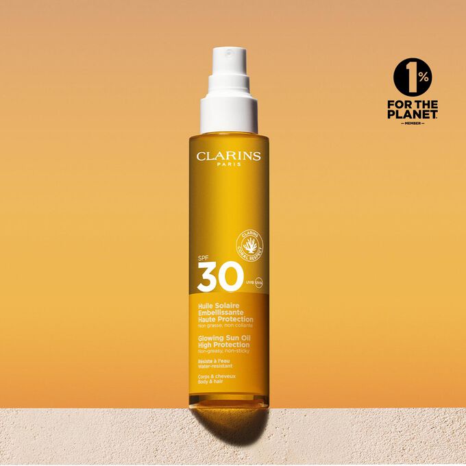 Plan produit d'une huile solaire corps et cheveux SPF30 en spray avec un message annonçant que Clarins s'engage en faveur de la protection de l'environnement