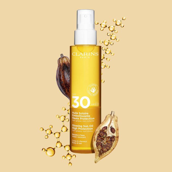 Plan produit de l'huile corps et cheveux SPF30 en spray orange à côté de fèves de cacao sur fond orange clair